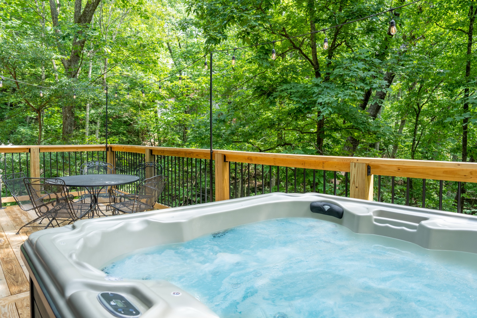 Private hot tub and patio table on Rustic Retreat's deck, surrounded by summer greenery