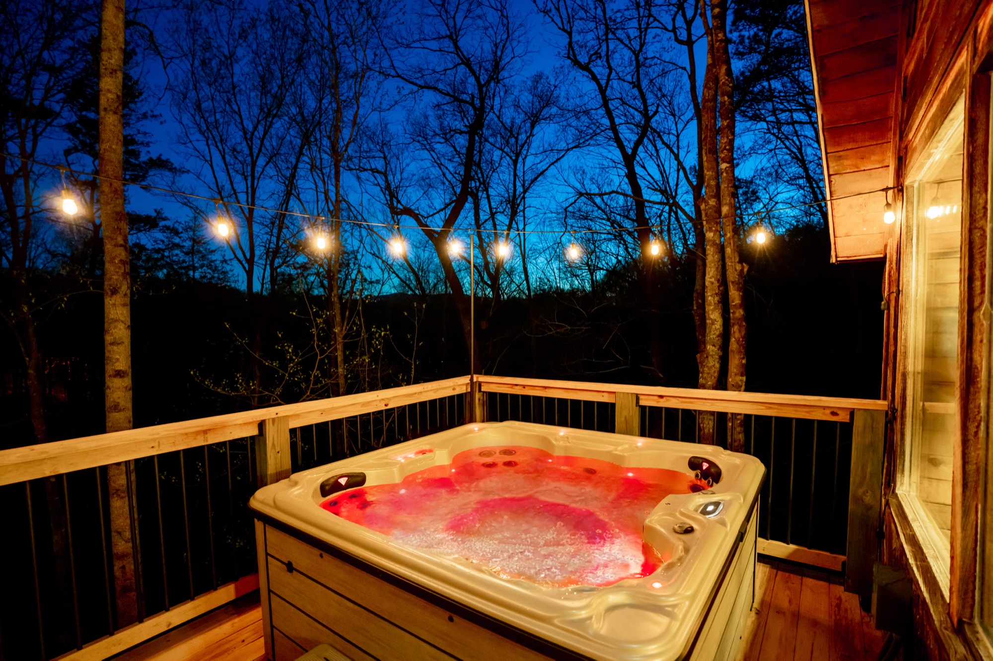 Rustic Retreat's hot tub glowing at dusk with string lights strung through the trees