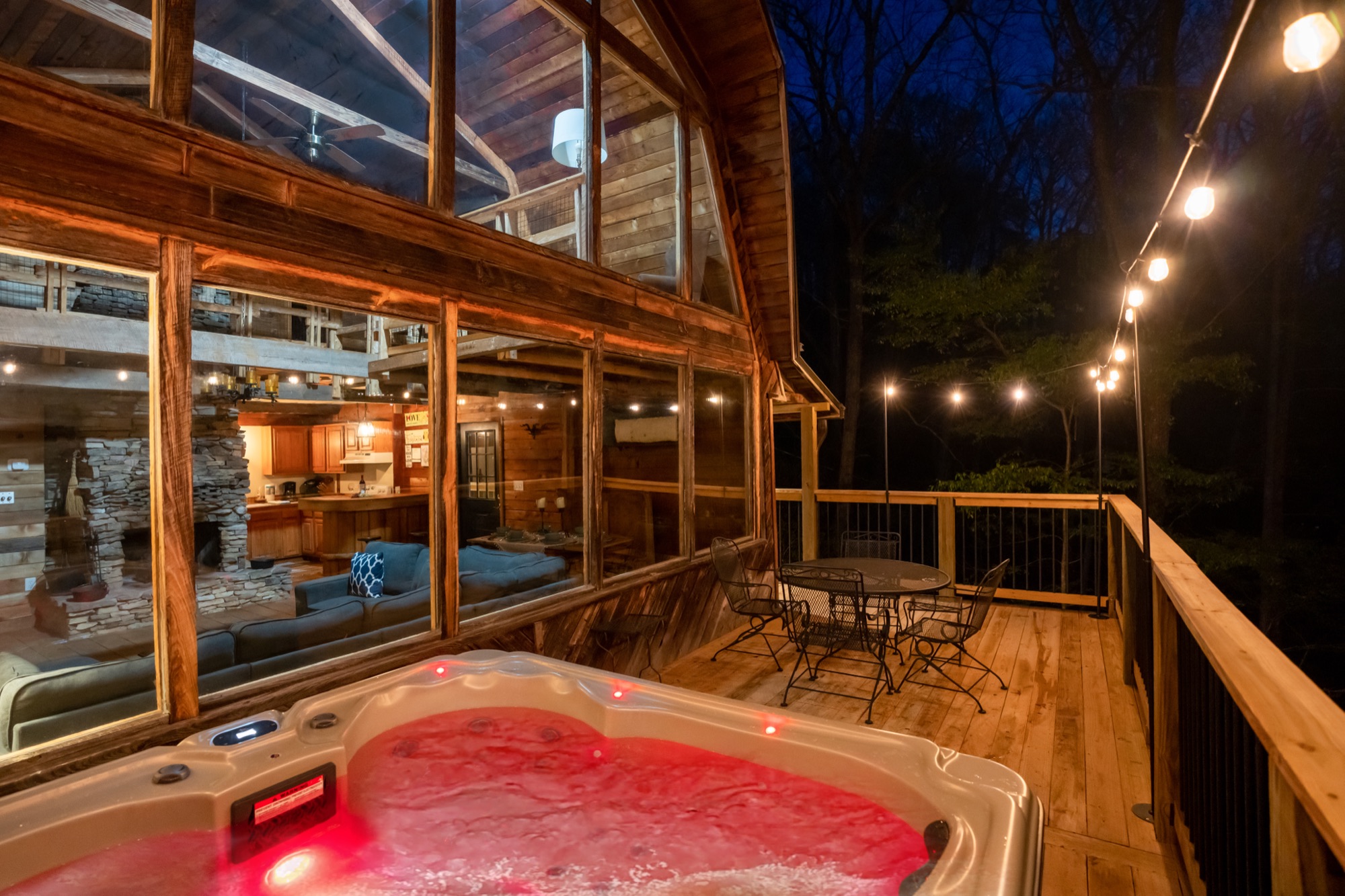 Rustic Retreat's screened deck hot tub glowing at night with the kitchen and living room visible through the windows