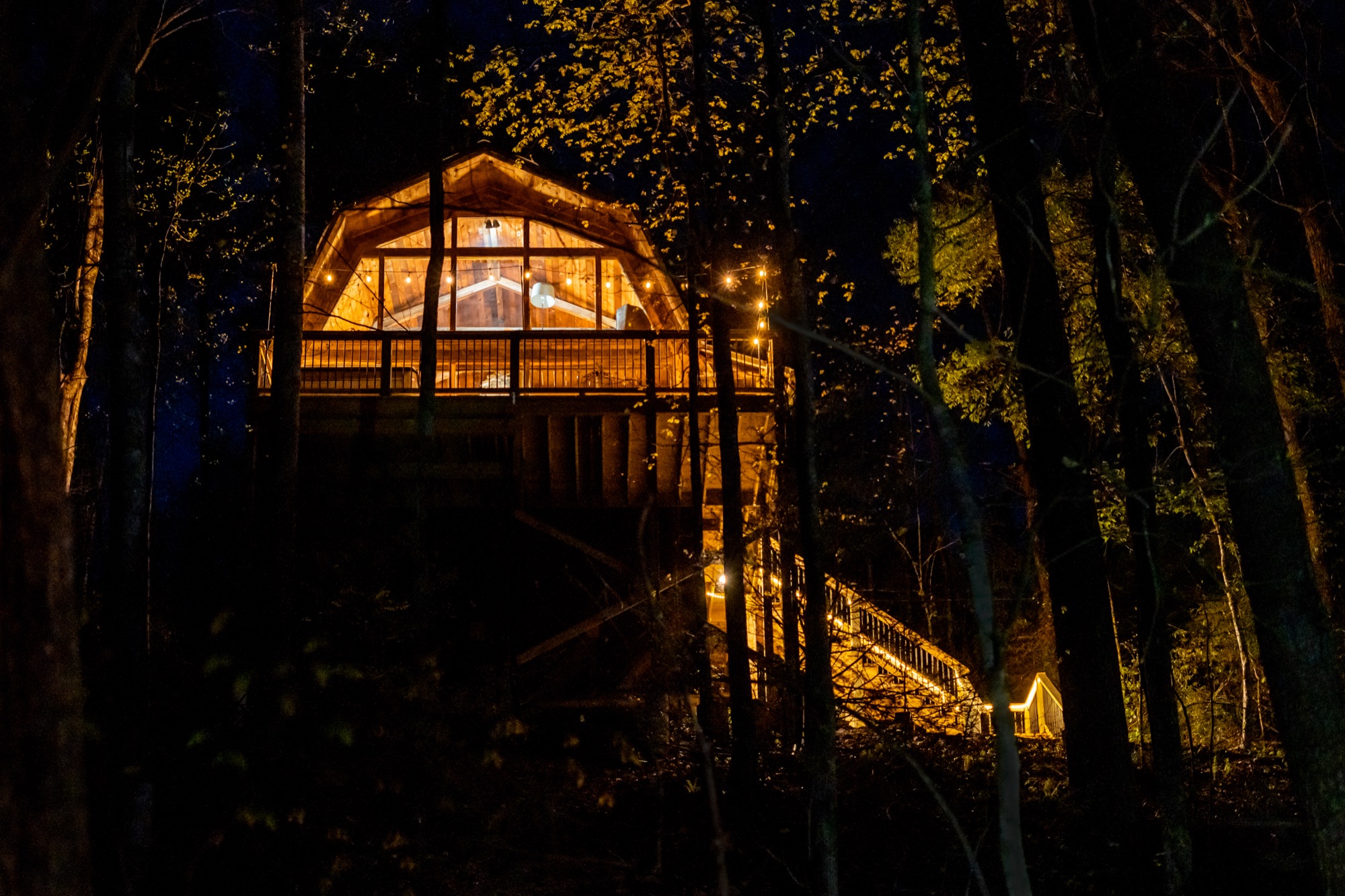 Rustic Retreat's exterior at night, with the hot tub deck visible through the trees