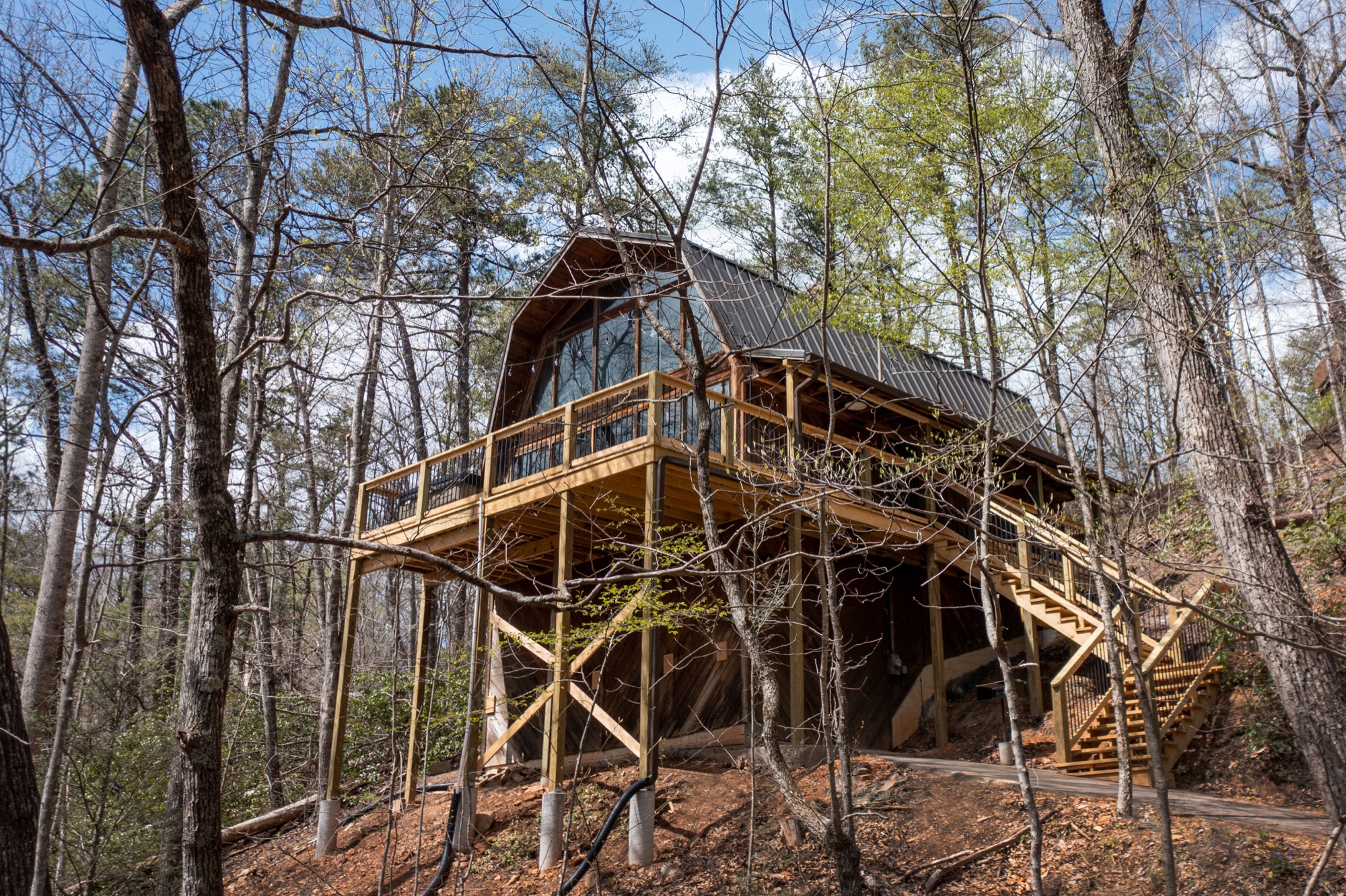 Rustic Retreat's chalet style A frame exterior with a full glass gable end, seen through surrounding trees